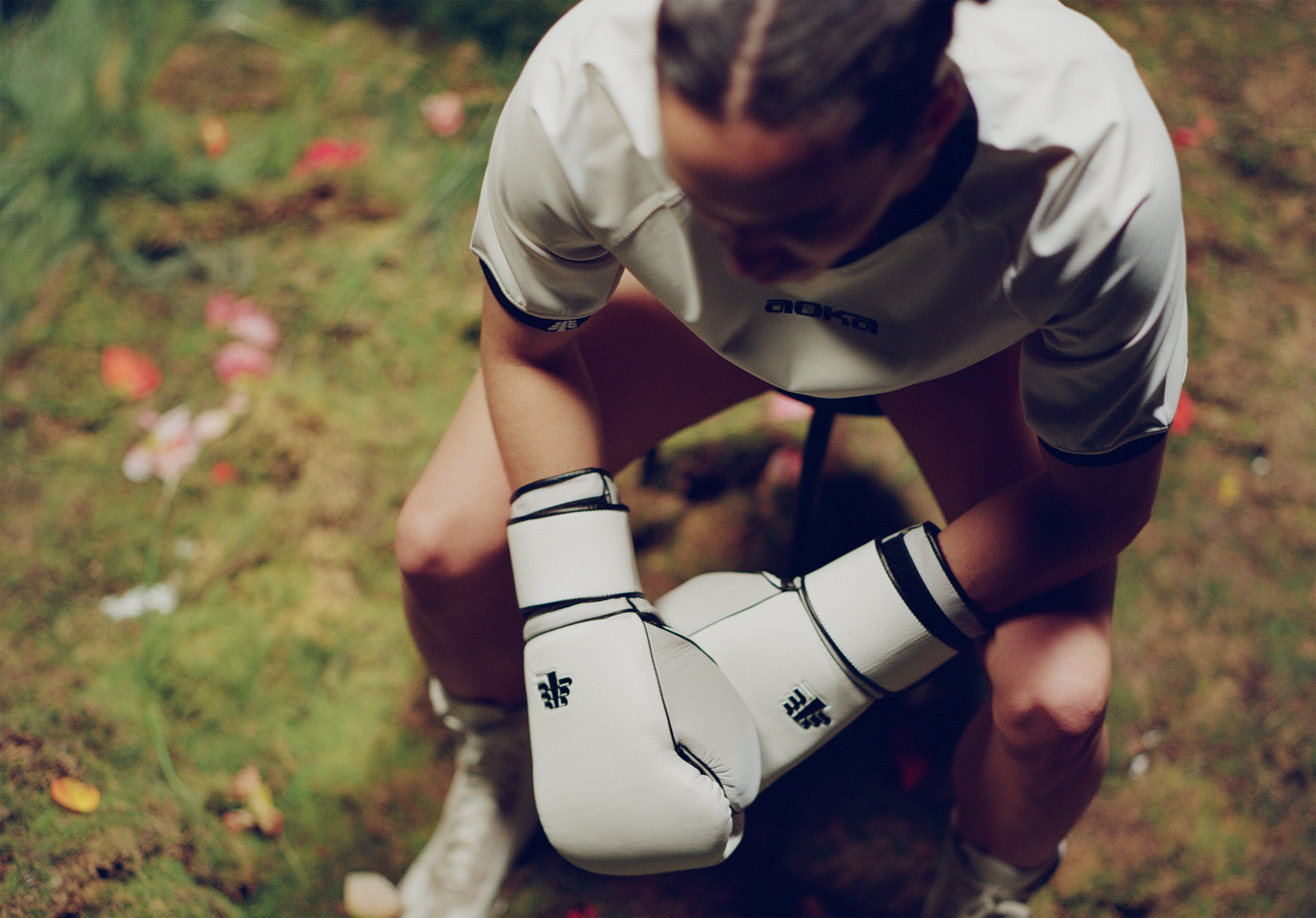 Person wearing white boxing gloves and a sports jersey, sitting on grass.